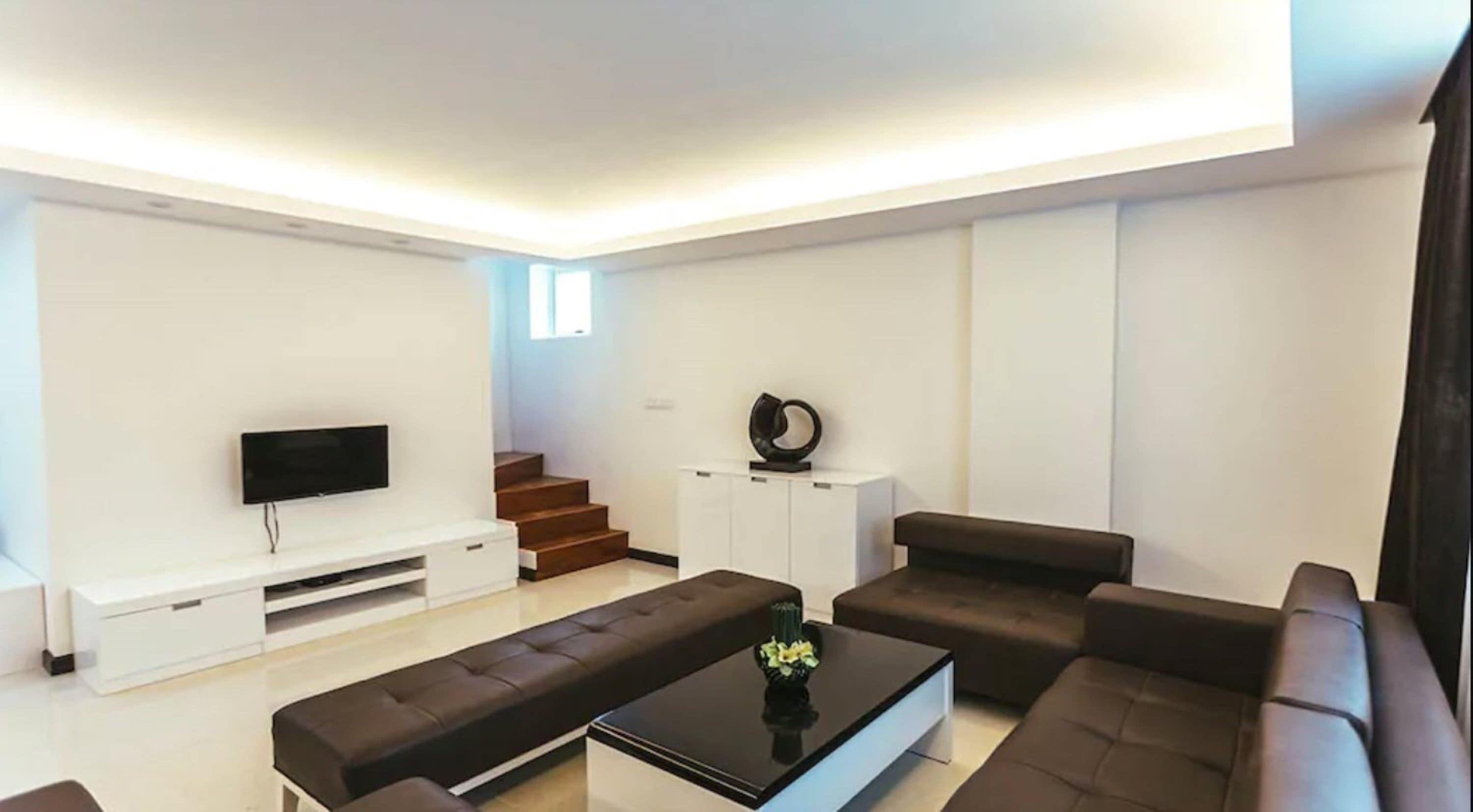 Un soggiorno moderno con una TV a schermo piatto, un divano, un tavolino da caffè e una scala che conduce a un piano superiore.