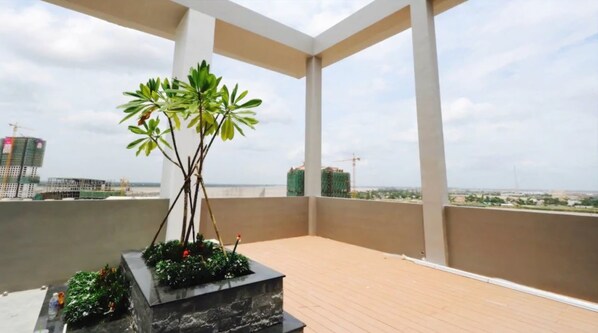 A balcony with a potted plant, a view of the cityscape, and a clear sky.