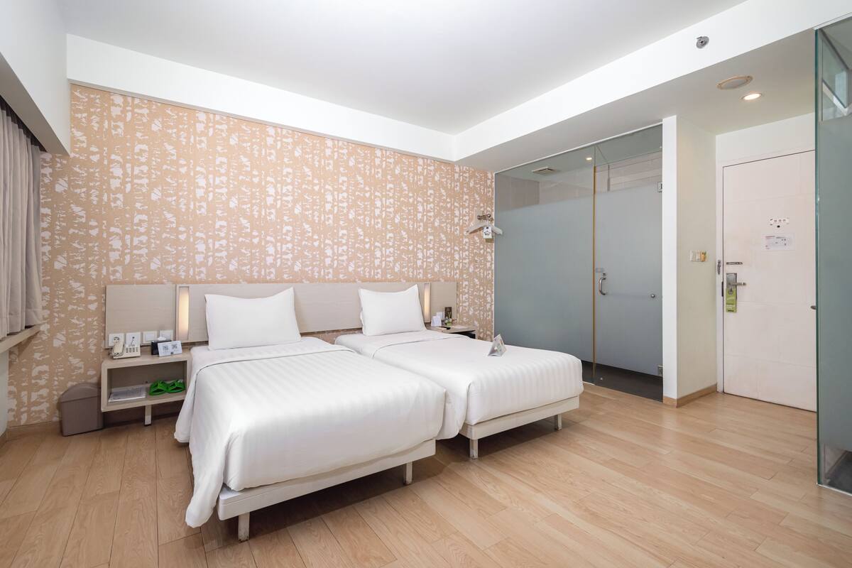 Ein modernes Hotelzimmer mit zwei Betten, einer Duschkabine aus Glas und Holzboden.