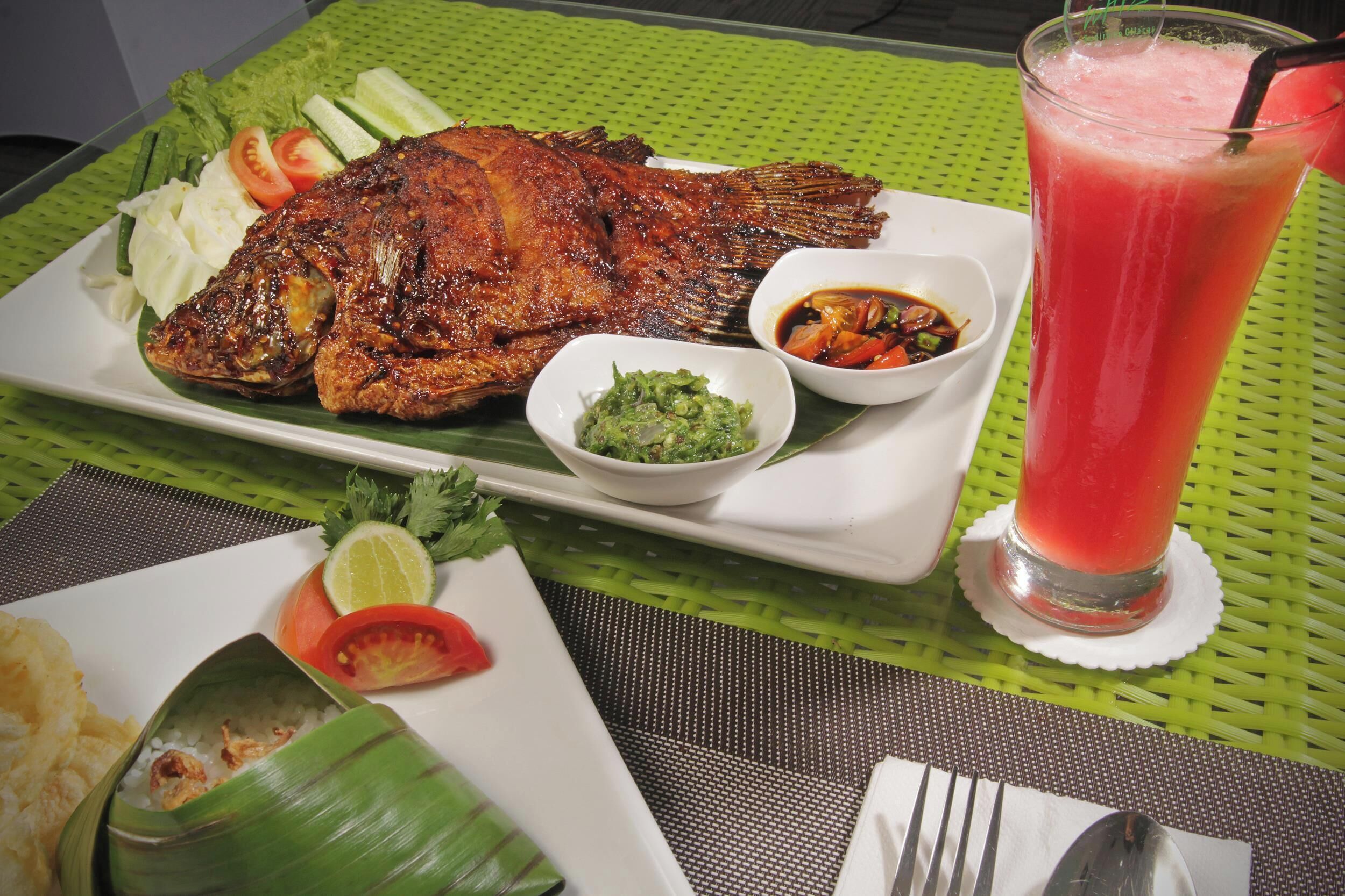 A meal with grilled fish, vegetables, and a drink on a table with a green placemat.