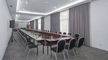 Una sala de conferencias con una larga mesa, sillas y una pantalla de proyector.