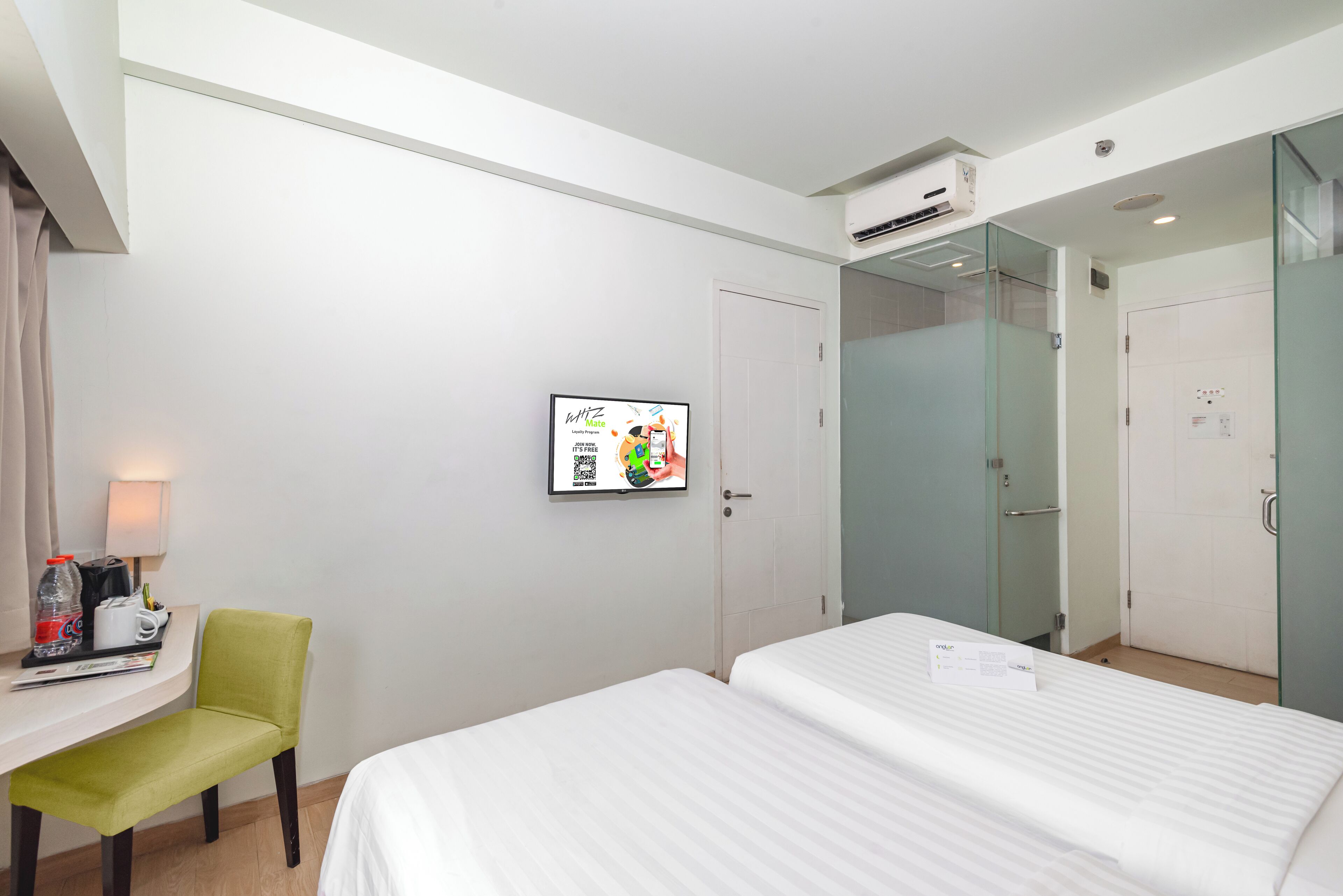 A hotel room with a bed, a desk, a chair, a shower, and a framed poster on the wall.