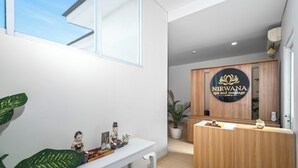 Un espace d’accueil avec un comptoir en bois, une plante en pot et une enseigne fixée au mur indiquant le spa et le centre de massage Nirvana.