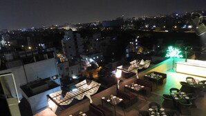 A rooftop restaurant with outdoor seating, a view of the cityscape at night, and a neon sign. - Urban Hermitage (Nagpur)