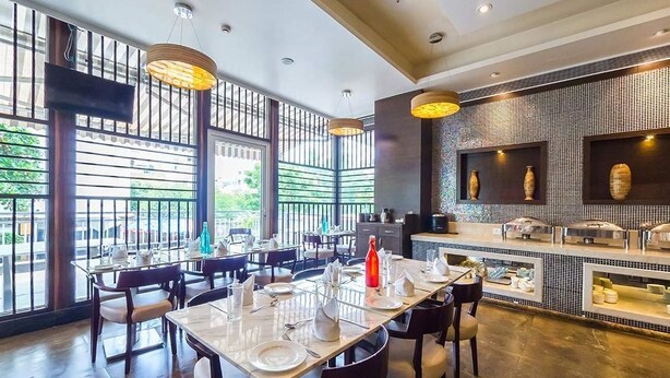 A dining area with tables set for service, a buffet counter with various dishes, and large windows allowing natural light. - Urban Hermitage (Nagpur)