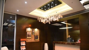 A hotel reception area with a modern design, featuring a marble reception desk, a chandelier, framed pictures on the wall, and a stack of white plates. - Urban Hermitage (Nagpur)