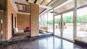 A lobby with a brick wall, a glass door entrance, and a seating area with chairs. - Urban Hermitage (Nagpur)