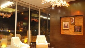 A lobby with two white armchairs, a marble floor, and a large window with a view of the city at night. - Urban Hermitage (Nagpur)