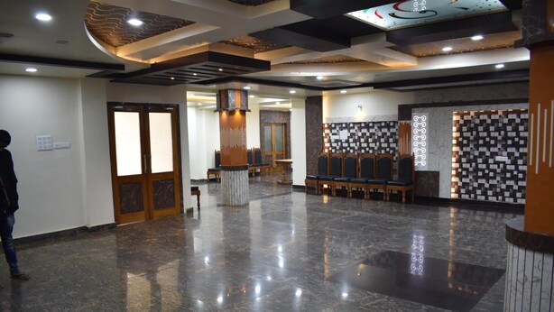 A spacious lobby with a polished marble floor, wooden doors, and a seating area with chairs and tables. - Hotel Rahil Palace (Varanasi)