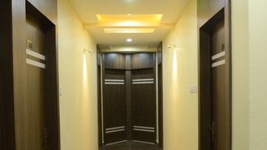 A hallway with wooden doors, a marble floor, and recessed lighting. - Hotel Rahil Palace (Varanasi)