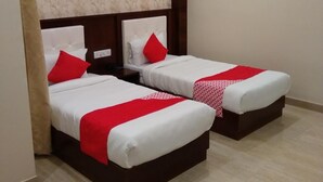 A hotel room with two beds, each with a red and white bedspread, a wooden headboard, and a marble-patterned wall above. - Hotel Rahil Palace (Varanasi)