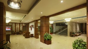 A spacious lobby with a high ceiling, wooden columns, comfortable seating, and potted plants. - Hotel Shoolin Grand (Guwahati)