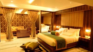 A spacious bedroom with a large bed, a sitting area with a sofa and armchairs, and a mirror reflecting the room. - Hotel Shoolin Grand (Guwahati)