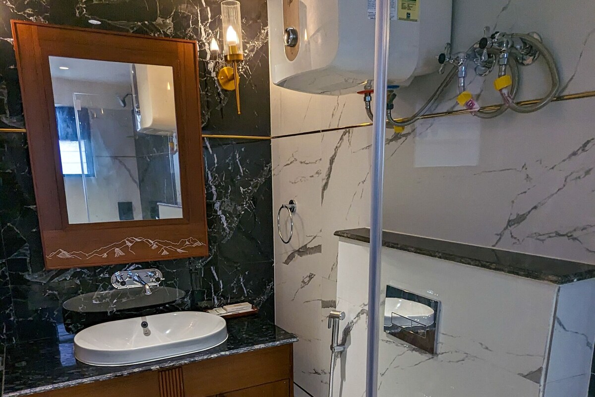 Een badkamer met een marmeren wastafel, een douche met glazen wanden en een wit toilet.