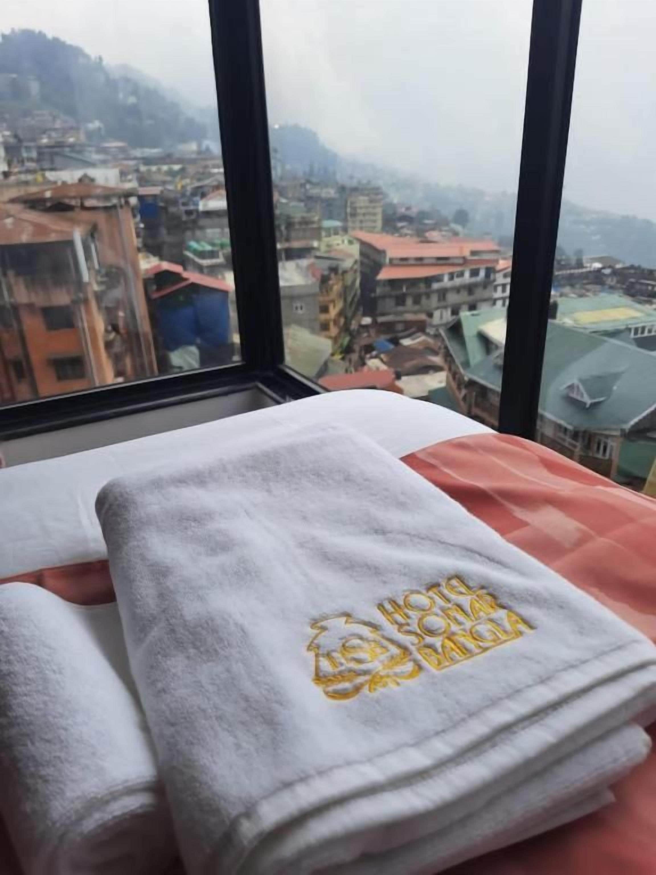 Una cama con una toalla blanca y un edredón rojo, una ventana con vistas a un paisaje urbano.