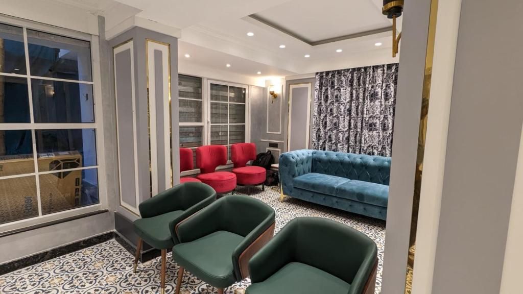 A room with a blue sofa, red chairs, and a green armchair. There are large windows and a patterned floor.