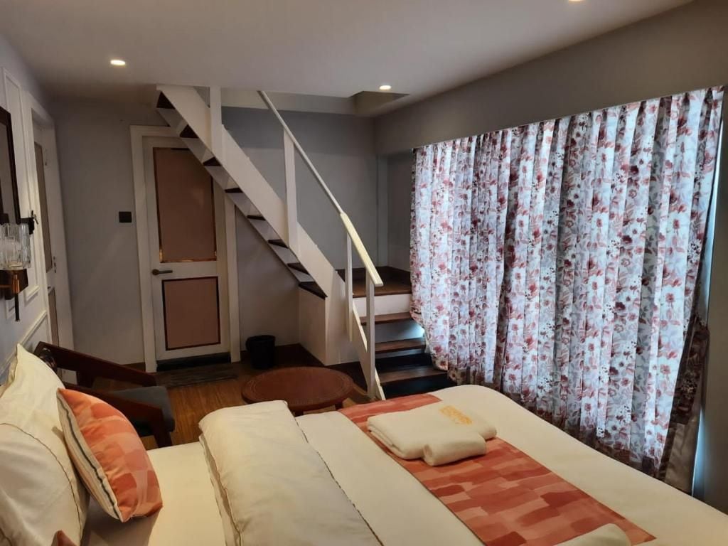 Quarto com cama, almofadas, mesa de cabeceira, janela com cortinas e escada.