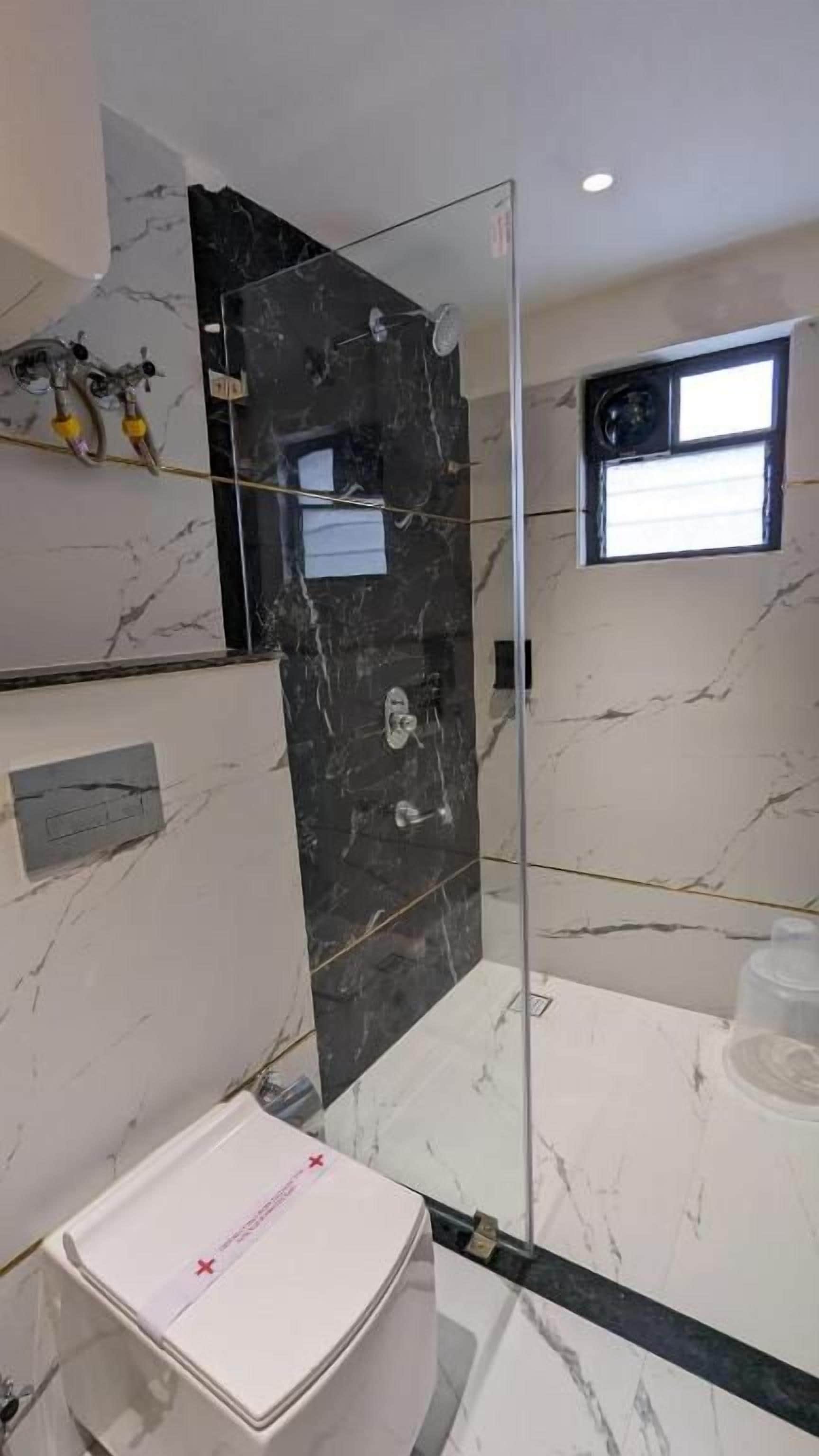 A modern bathroom with a glass shower enclosure, marble walls, and a white sink.