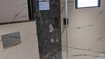 Un baño moderno con cabina de ducha de vidrio, paredes de mármol y lavamanos blanco.
