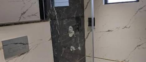 A modern bathroom with a glass shower enclosure, marble walls, and a white sink.