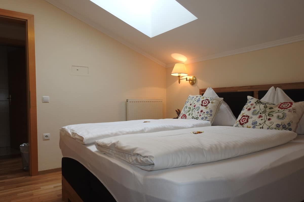 A hotel room with two beds, a skylight, a wall-mounted lamp, and a radiator.