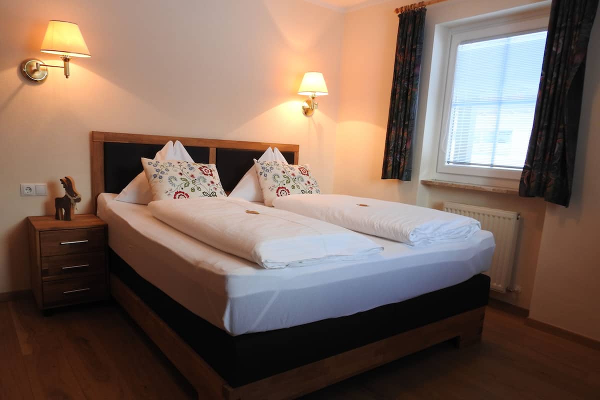 A double bed with floral pillows, a nightstand with drawers, two wall-mounted lamps, and a window with curtains.