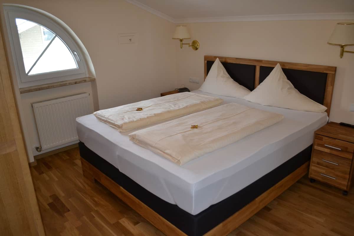 A neatly made bed with a wooden headboard, a bedside table, a lamp, and a window with a view of the outside.