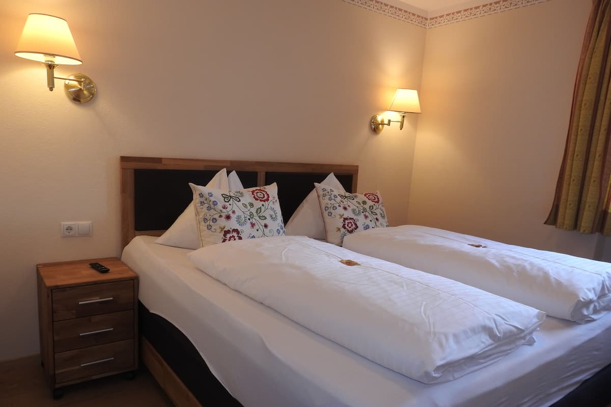 A double bed with white linens and floral-patterned pillows, two bedside tables with lamps, and a wooden headboard.