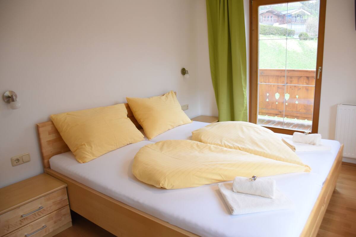 Una cama con almohadones amarillos, cabecera de madera y cortina verde.