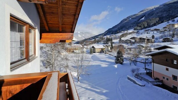 A wooden balcony with a view of a snow-covered village and mountains in the background. - Hotel Valerie (Saalbach-Hinterglemm)