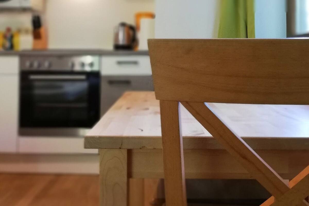 Una cocina con armarios blancos, una mesa de madera y una cortina verde.