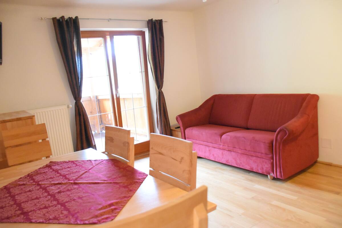 Una habitación con una cama de madera, un sofá rojo y una ventana con cortinas.