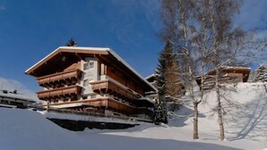 A multi-story wooden chalet with balconies, set against a snowy mountain backdrop. - Hotel Valerie (Saalbach-Hinterglemm)