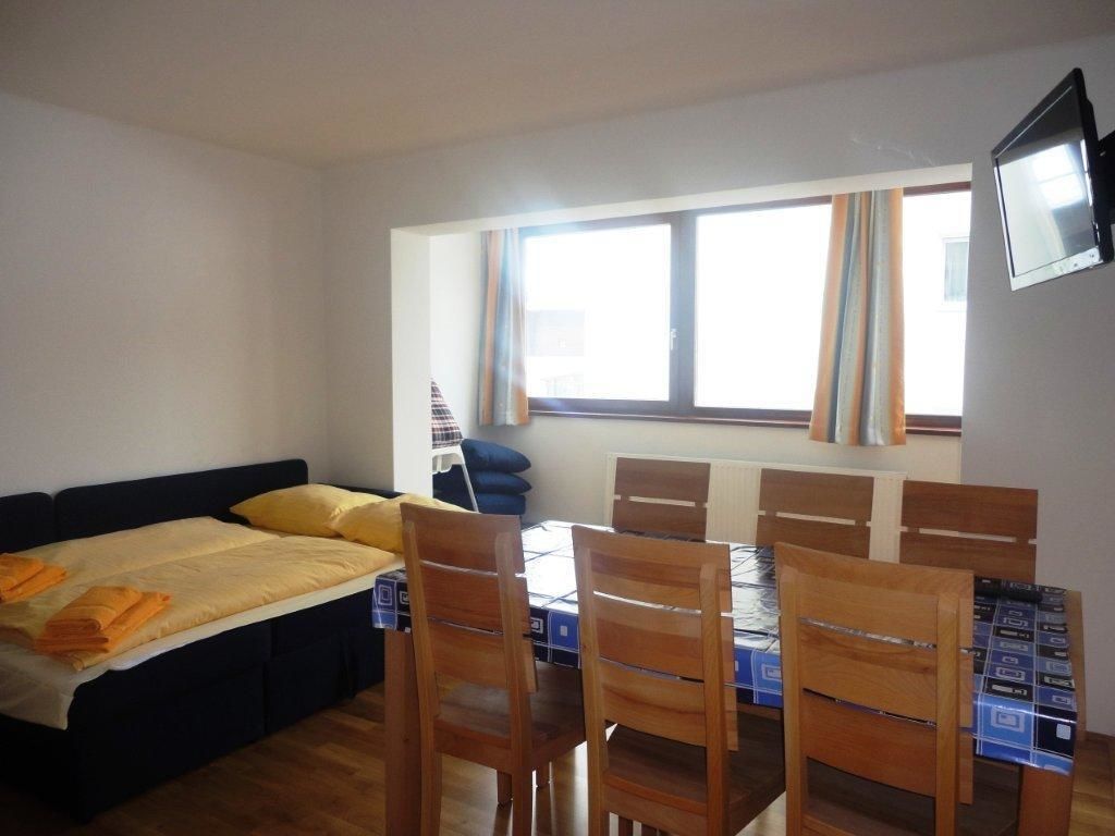 Ein Zimmer mit einem Bett, einem Esstisch mit Stühlen, einem an der Wand befestigten Fernseher und einem Fenster mit Vorhängen.