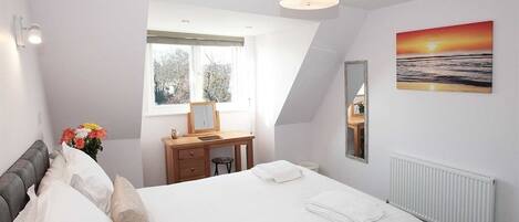 Un dormitorio con cama, escritorio, silla, ventana, radiador y un cuadro en la pared.