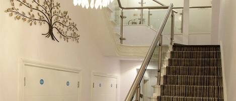 A staircase with a striped carpet, a metal handrail, and a wall-mounted tree decoration.