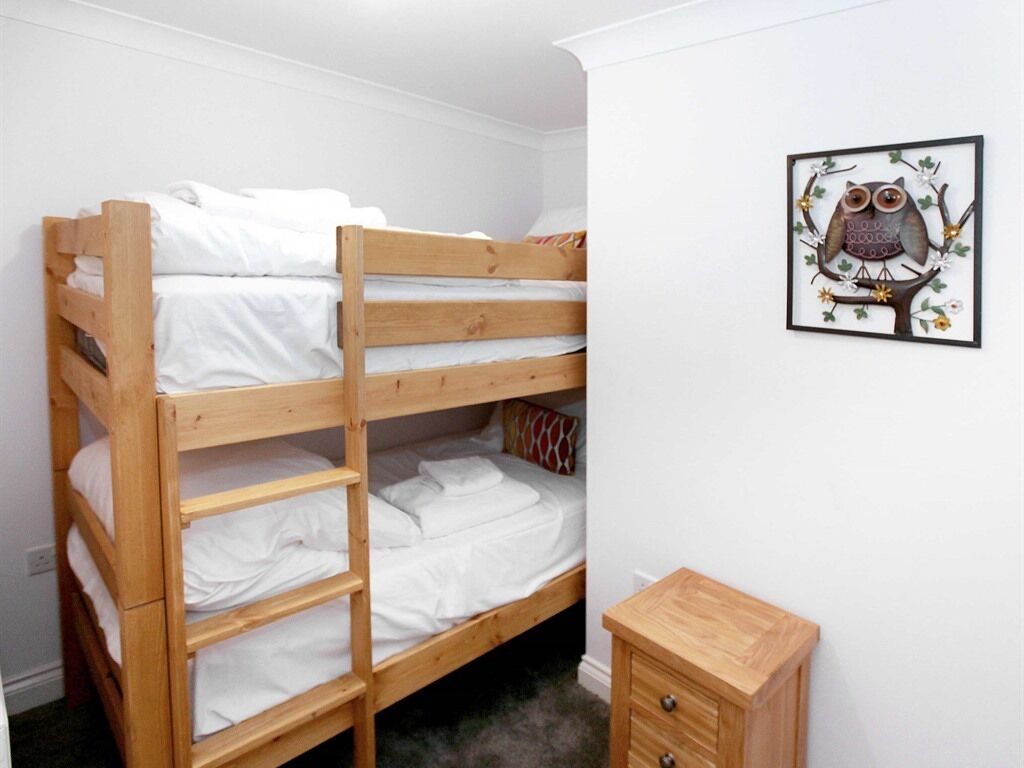 A bunk bed with white bedding, a small wooden cabinet, and a framed owl artwork on the wall.