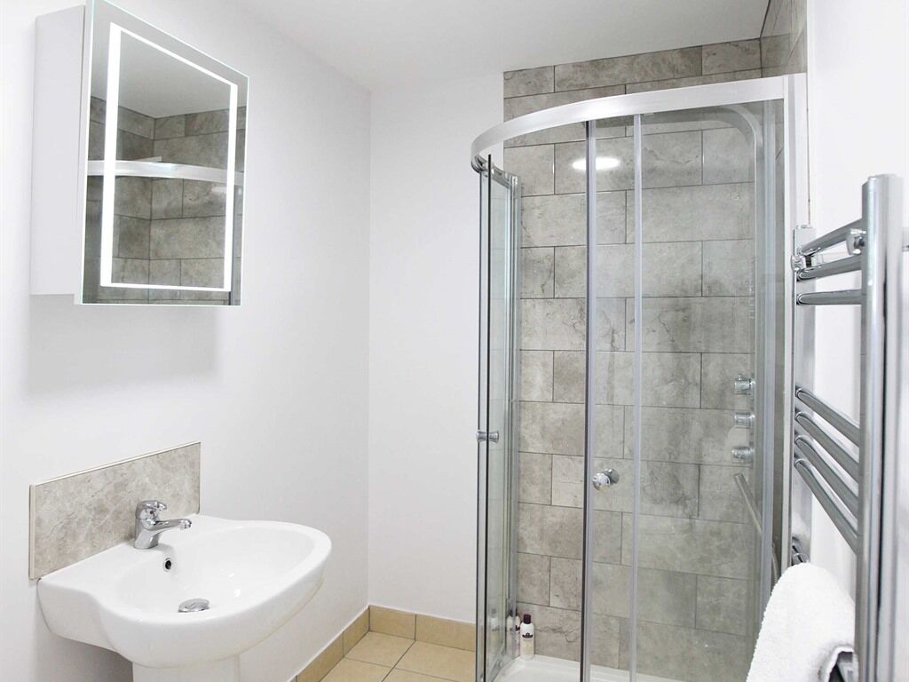Une salle de bain moderne avec une douche à parois de verre, un lavabo blanc et un meuble avec des portes miroir.