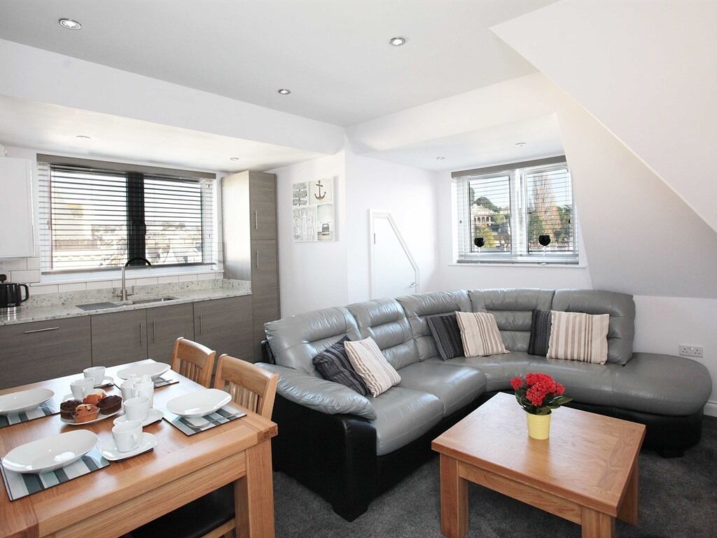 A modern living room with a grey sectional sofa, a wooden coffee table, and a dining area with a table set for two.