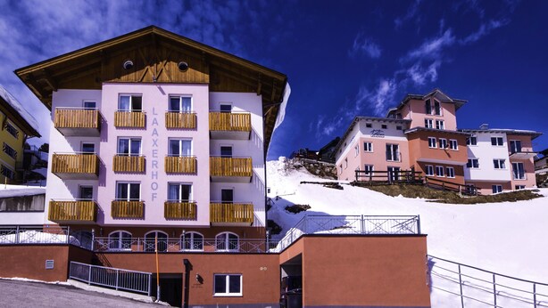 Un immeuble à plusieurs étages doté de balcons, d’un espace de stationnement et d’une pente recouverte de neige.