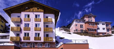 Un edificio de varios pisos con balcones, un área de estacionamiento y una pendiente cubierta de nieve.