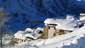 Un village de montagne enneigé, avec des bâtiments de style chalet, un télésiège et un ciel d’un bleu limpide.