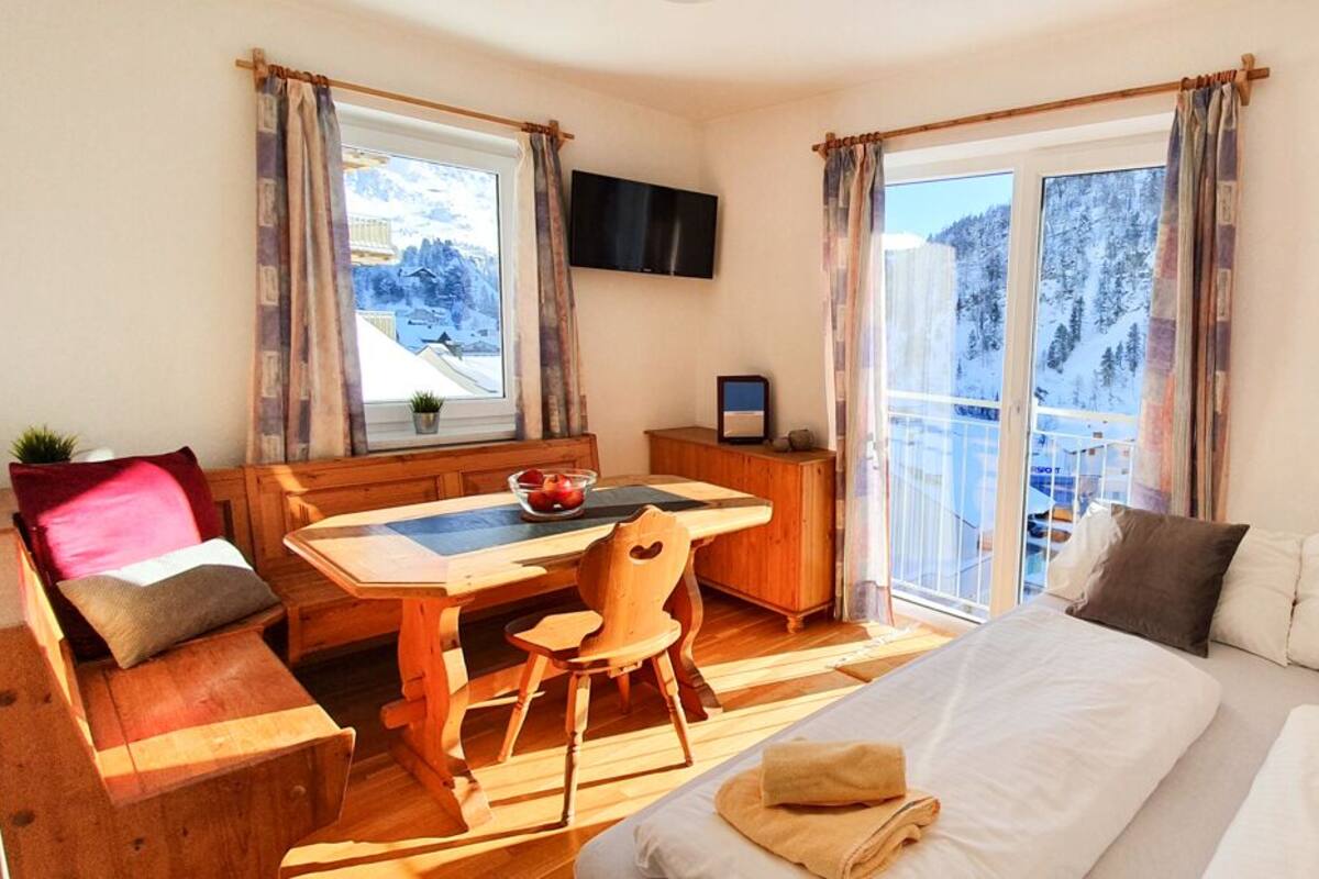 Um quarto aconchegante com uma cama, uma mesa de madeira, uma cadeira, um banco e uma TV.