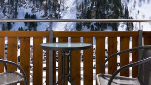 Un balcon avec deux fauteuils en osier et une petite table, d’où l’on peut admirer une montagne enneigée et une zone boisée.