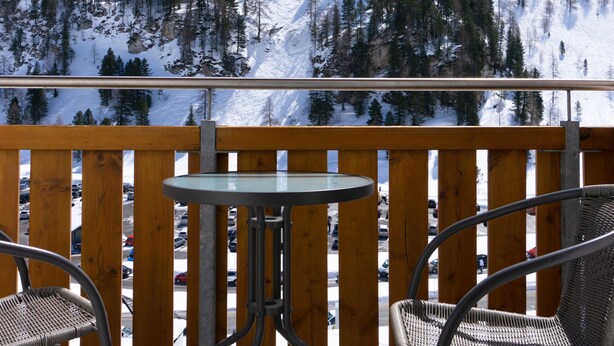 Un balcon avec deux fauteuils en osier et une petite table, d’où l’on peut admirer une montagne enneigée et une zone boisée.