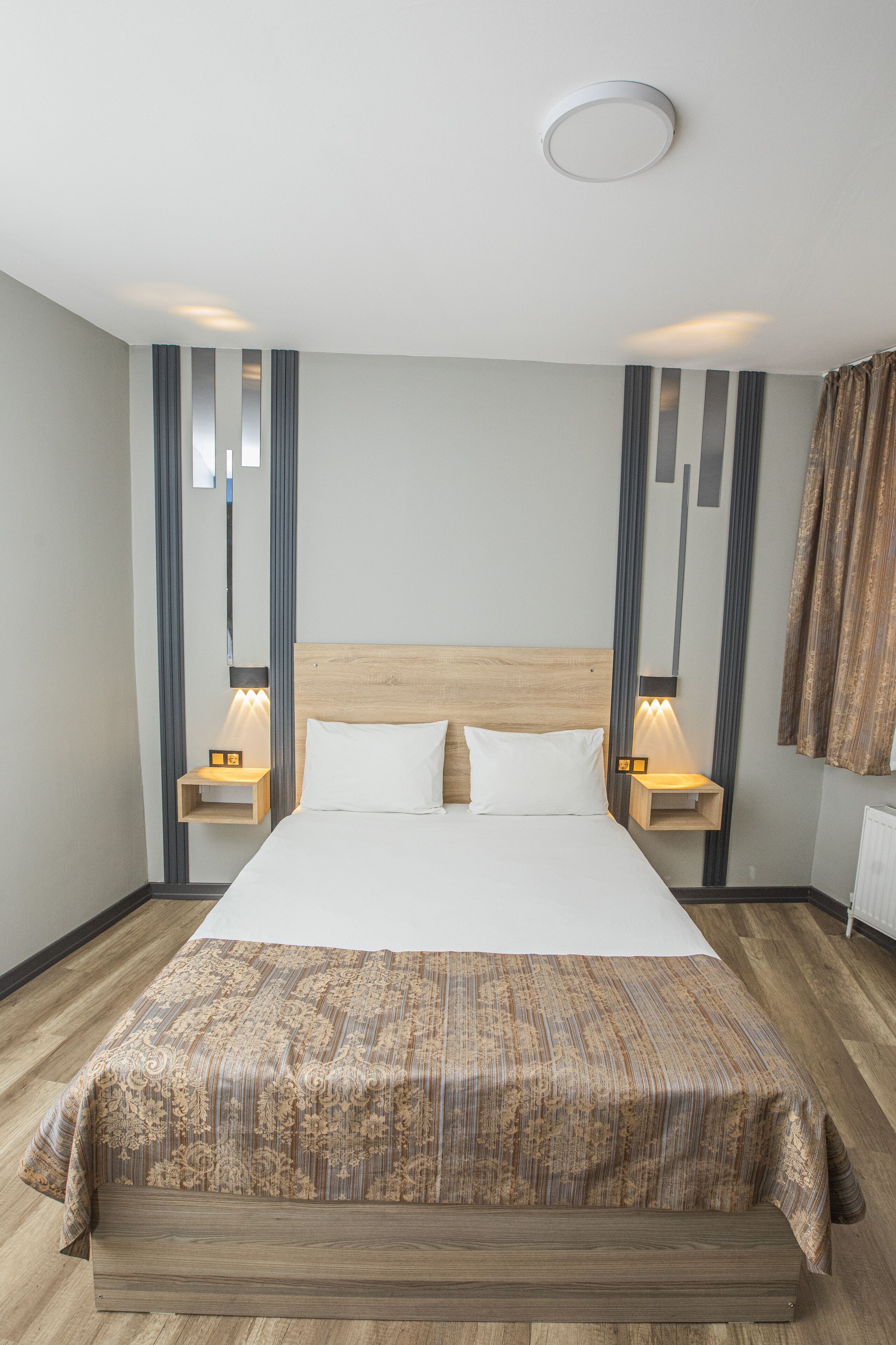 Una habitación de hotel moderna con una cama grande, un cabecero de madera y dos mesitas de noche con lámparas.