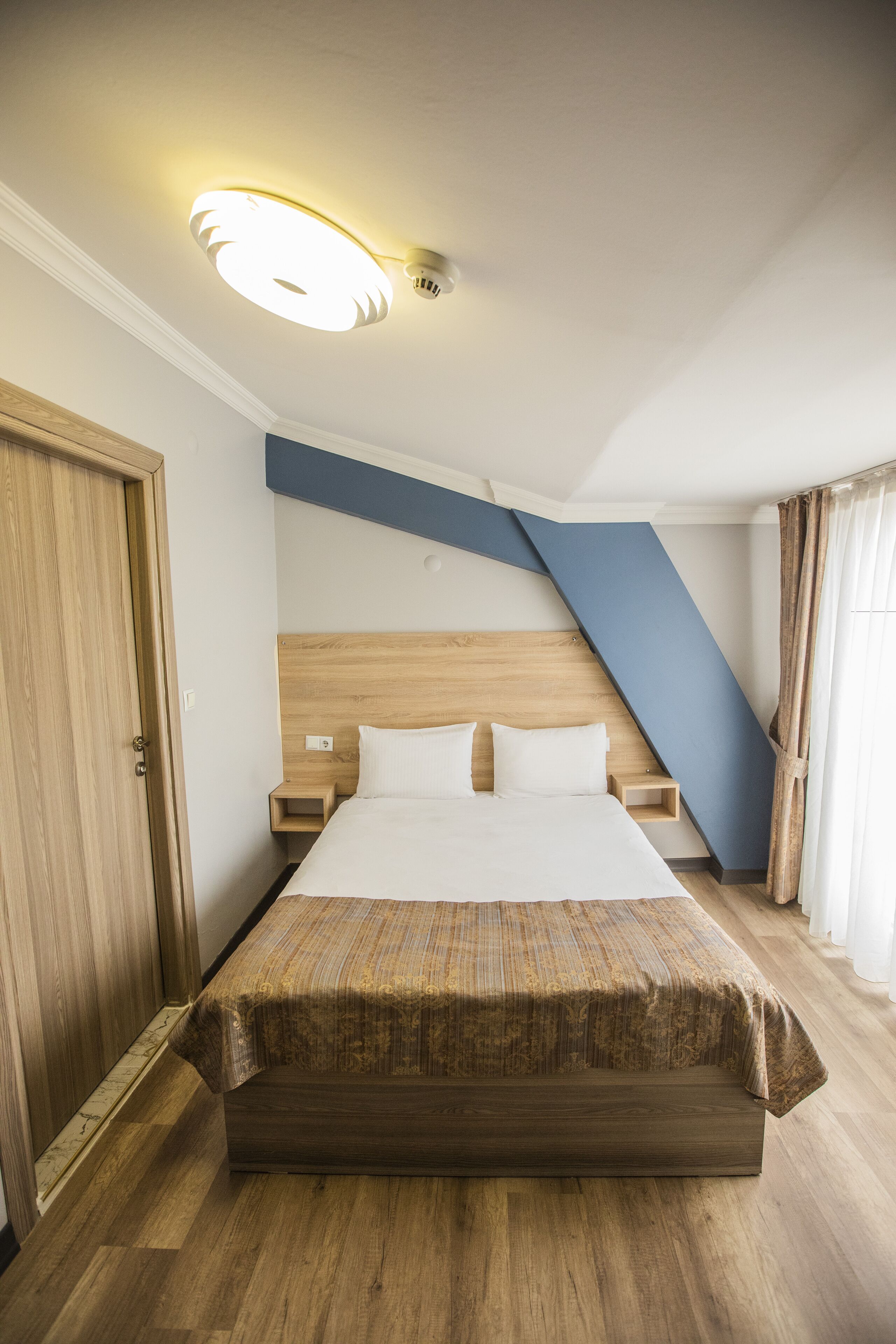Camera d'albergo con un letto, una testiera in legno, comodini e un soffitto spiovente.