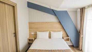 Camera d'albergo con un letto, una testiera in legno, comodini e un soffitto spiovente.