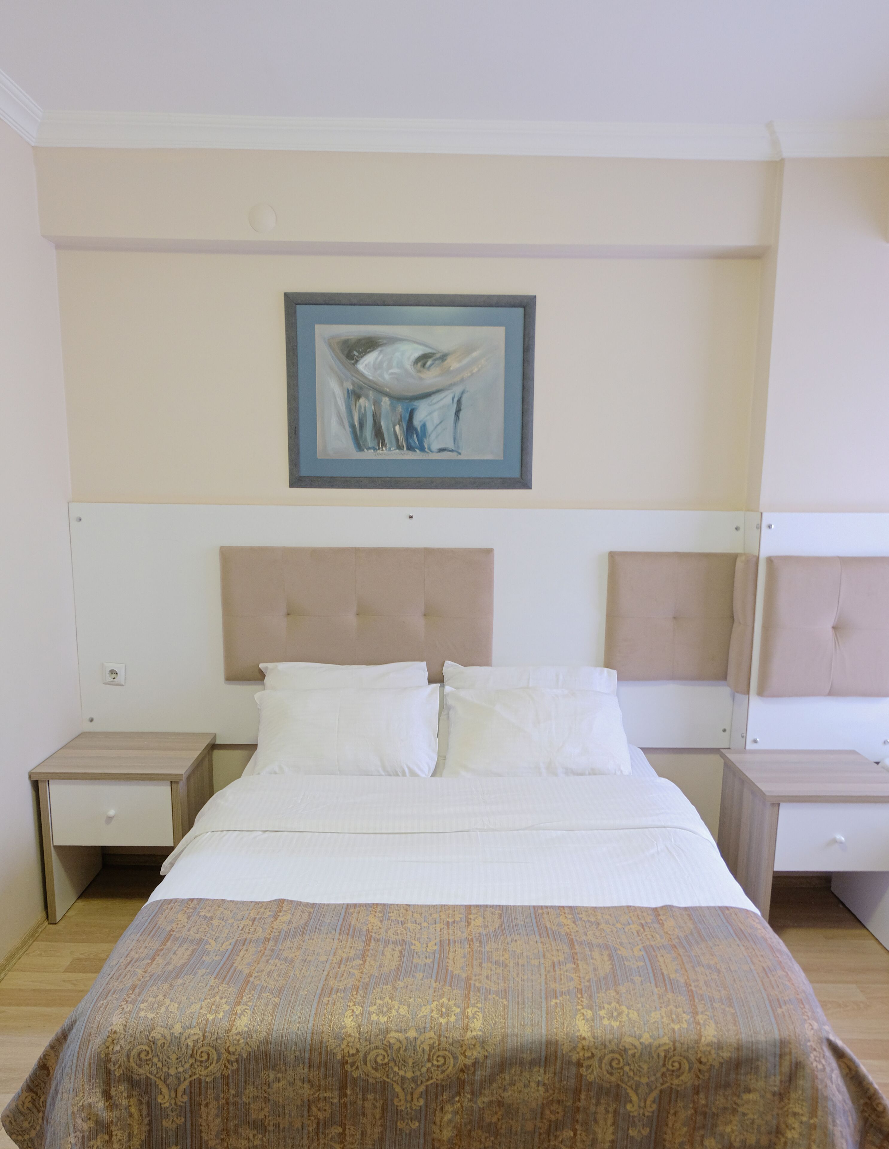 Habitación de hotel con cama, dos mesitas de noche, cabecera y un cuadro enmarcado en la pared.