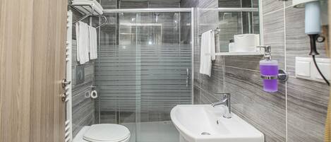 Un baño moderno con ducha de vidrio, lavamanos blanco y retrete.